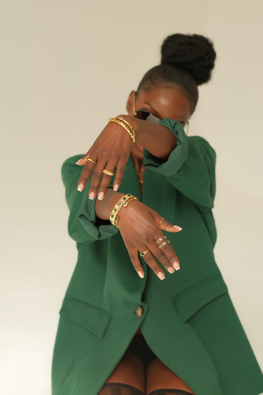 Person wearing a green outfit with gold jewelry against a plain background