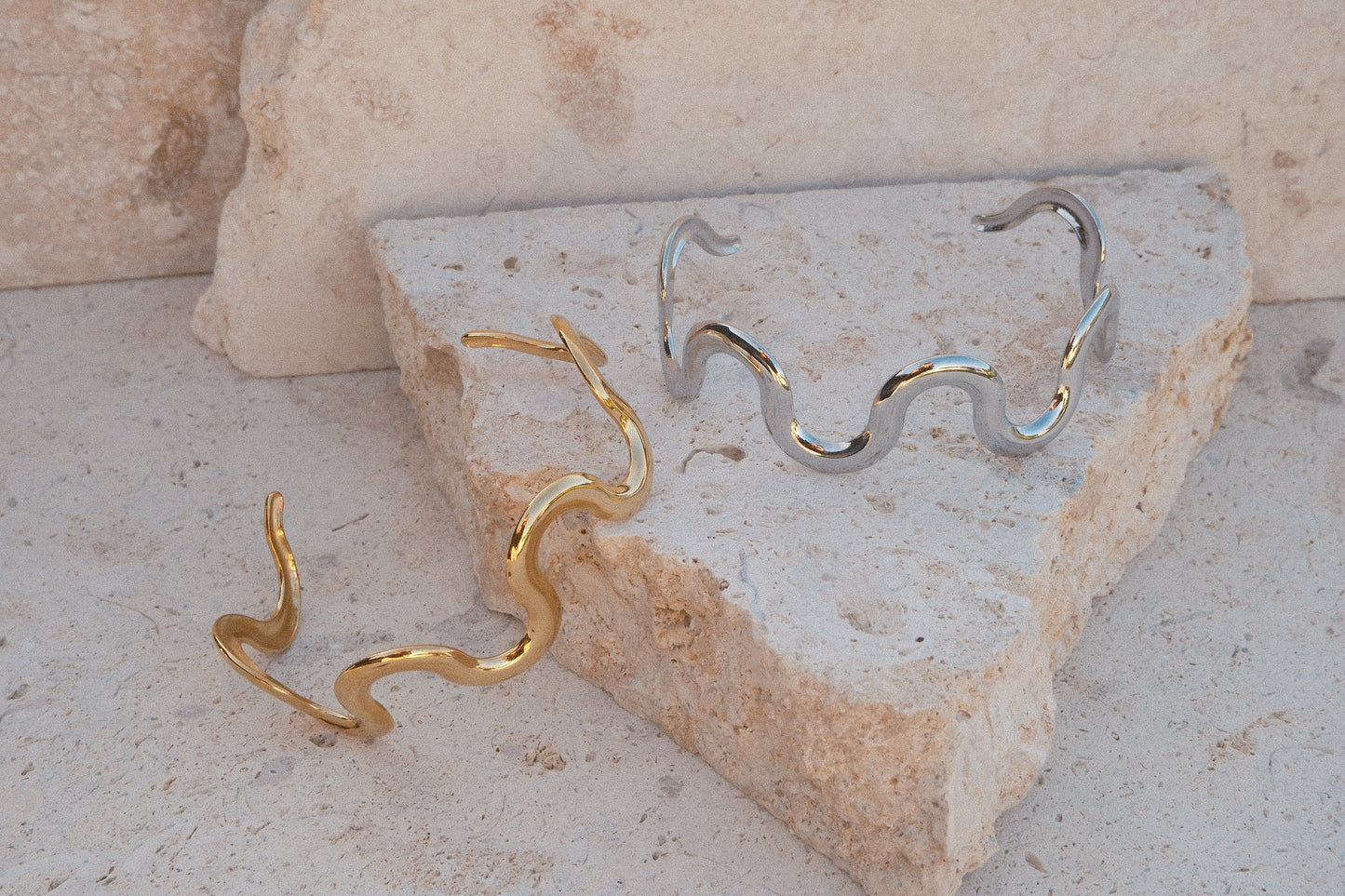 Gold and silver wave-shaped bracelets on a stone surface