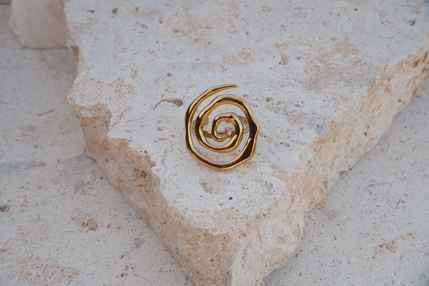 Gold spiral earring on a textured stone surface