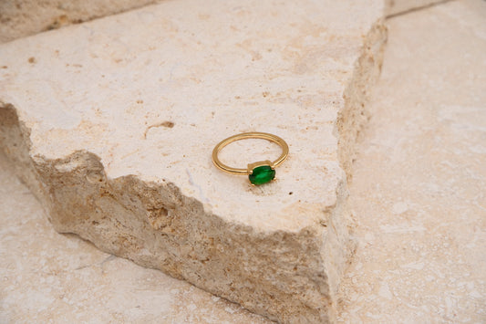 Gold ring with a green gemstone on a textured stone surface