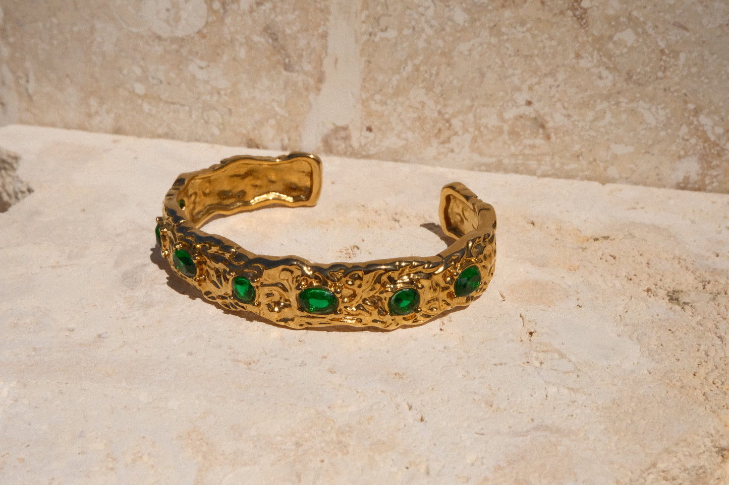 Gold bracelet with green gemstones on a textured surface