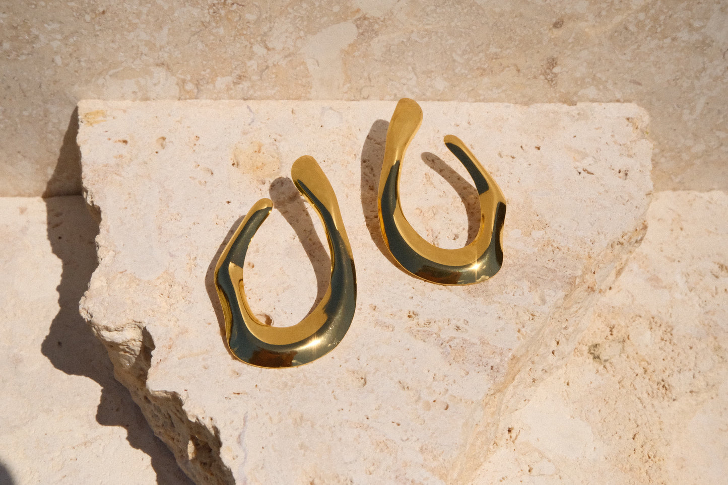 Gold and green hoop earrings on a textured stone surface