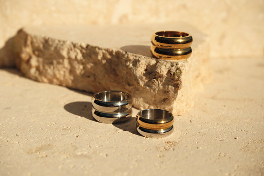 Three rings, two gold and one silver, stacked on a textured stone surface.