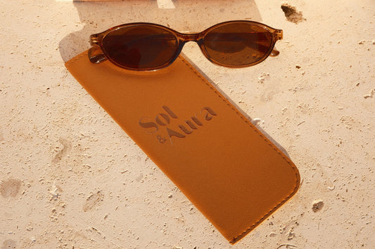 Brown sunglasses on a matching brown case with 'Sol & Aura' text, on a tiled surface.