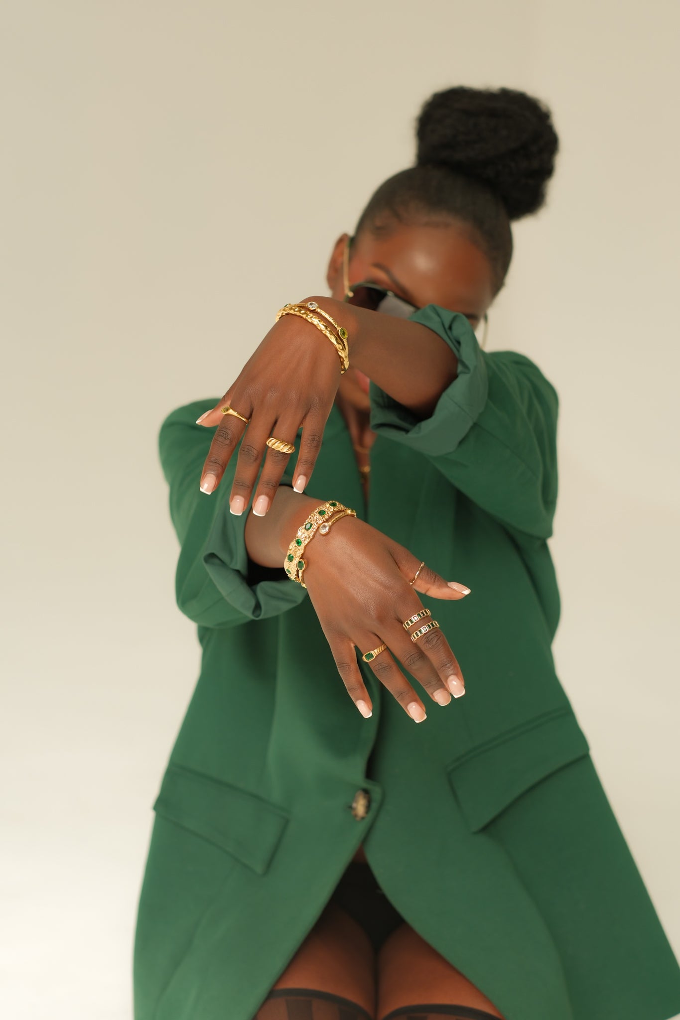 Person wearing a green outfit with gold jewelry against a plain background