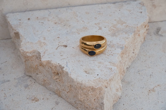Gold ring with black stones on a textured stone surface