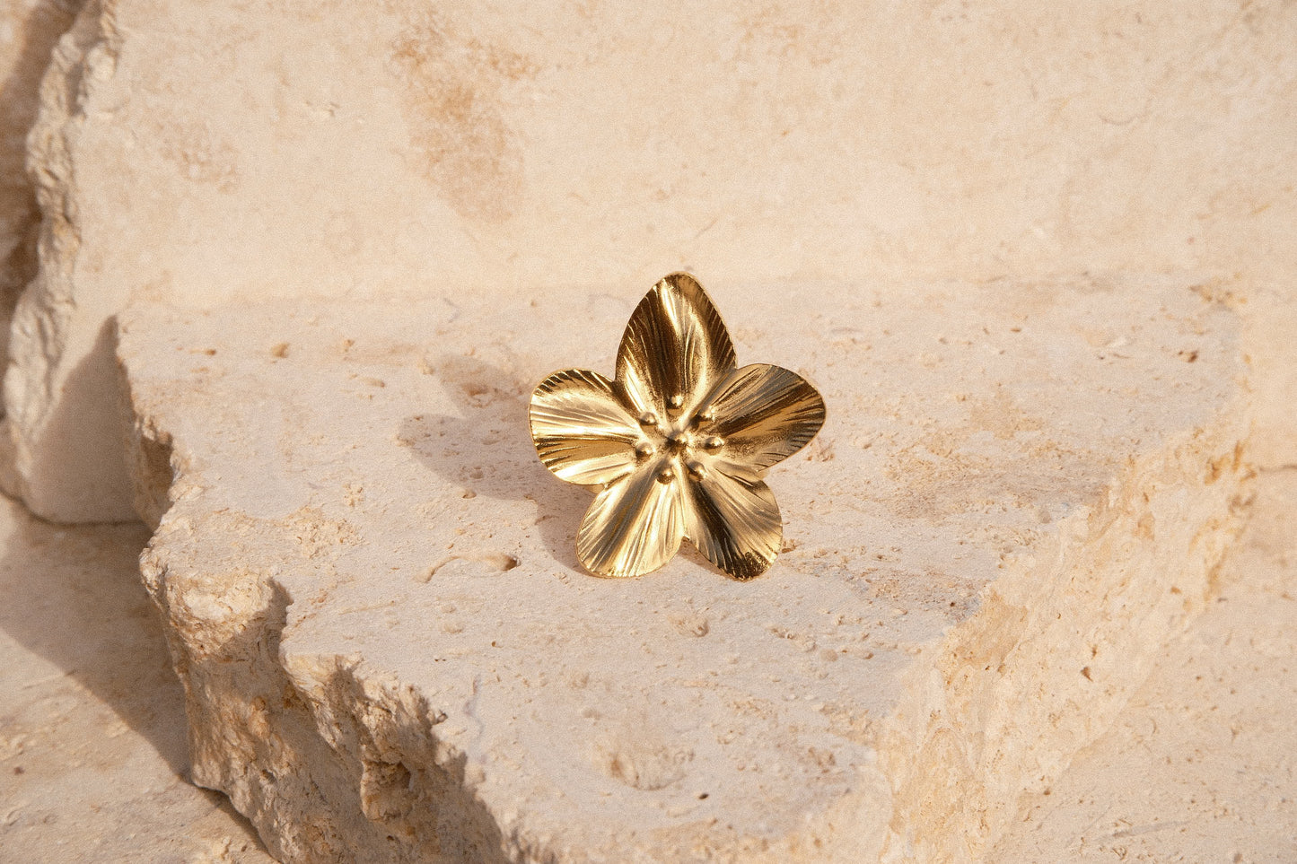 Gold flower-shaped earring on a textured beige stone surface