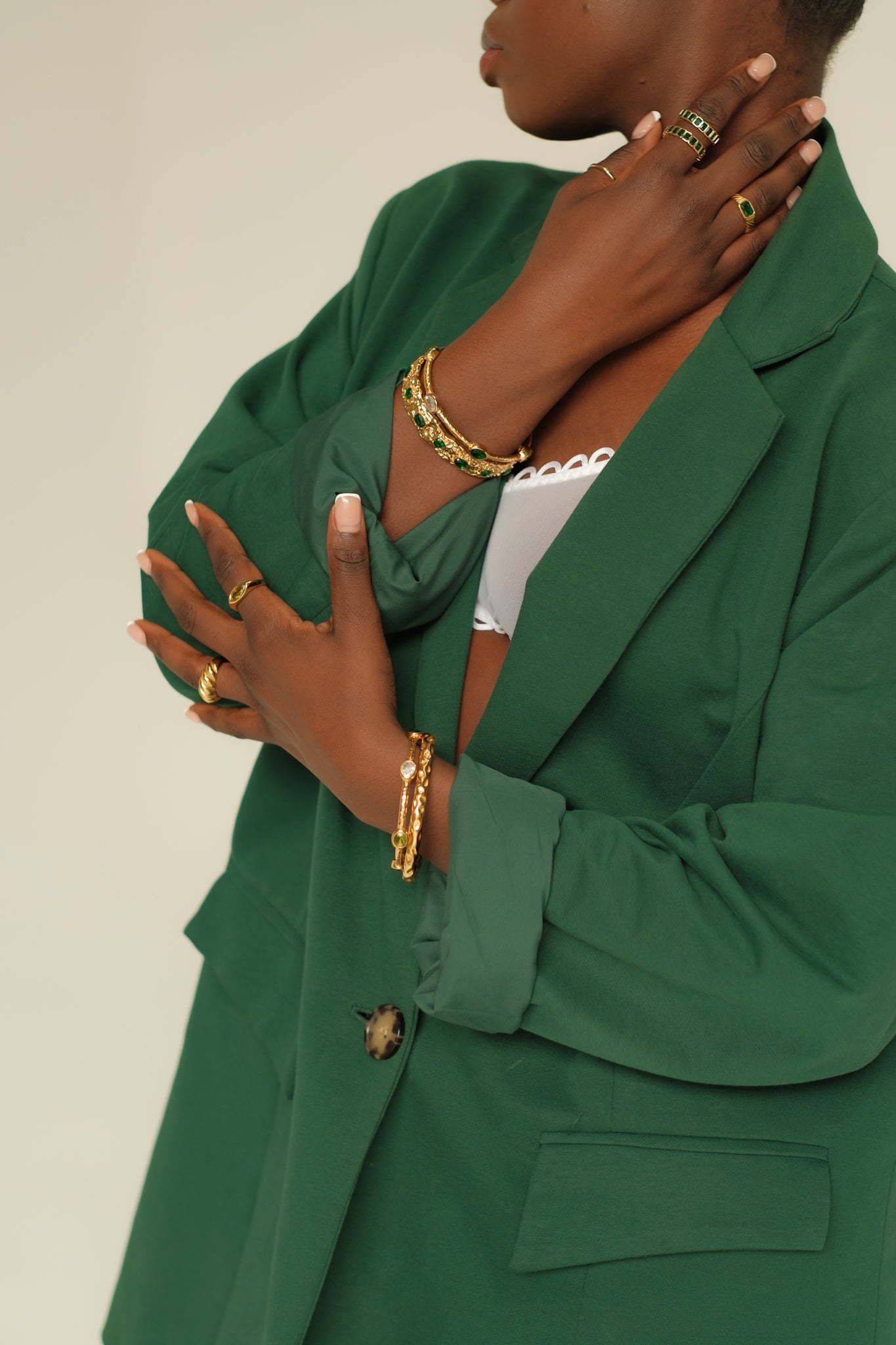 Person wearing a green blazer with gold jewelry on a neutral background