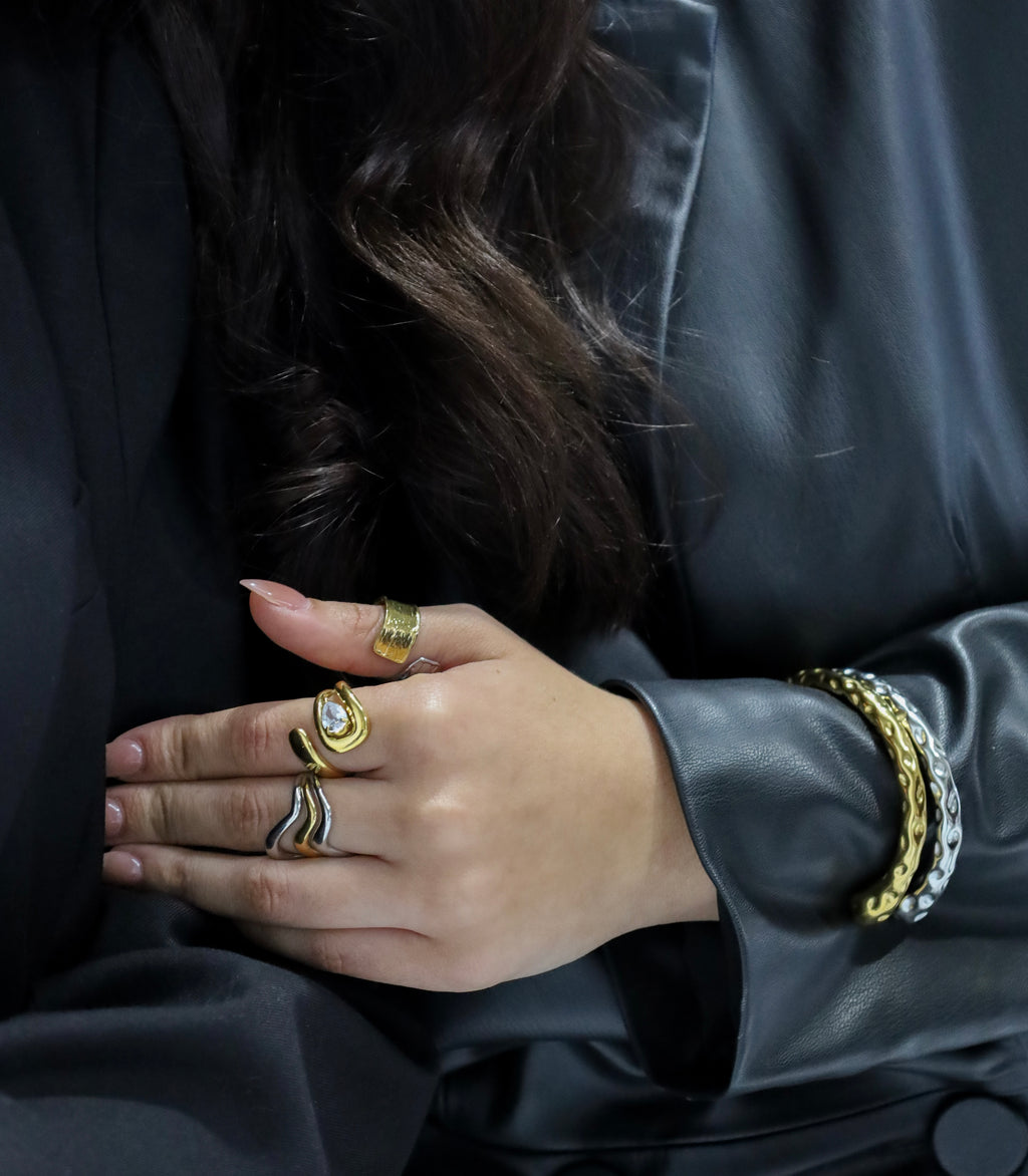 Close-up of a person's hand wearing multiple gold rings and bracelets against a dark background