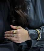 Close-up of a person's hand wearing multiple gold rings and bracelets against a dark background