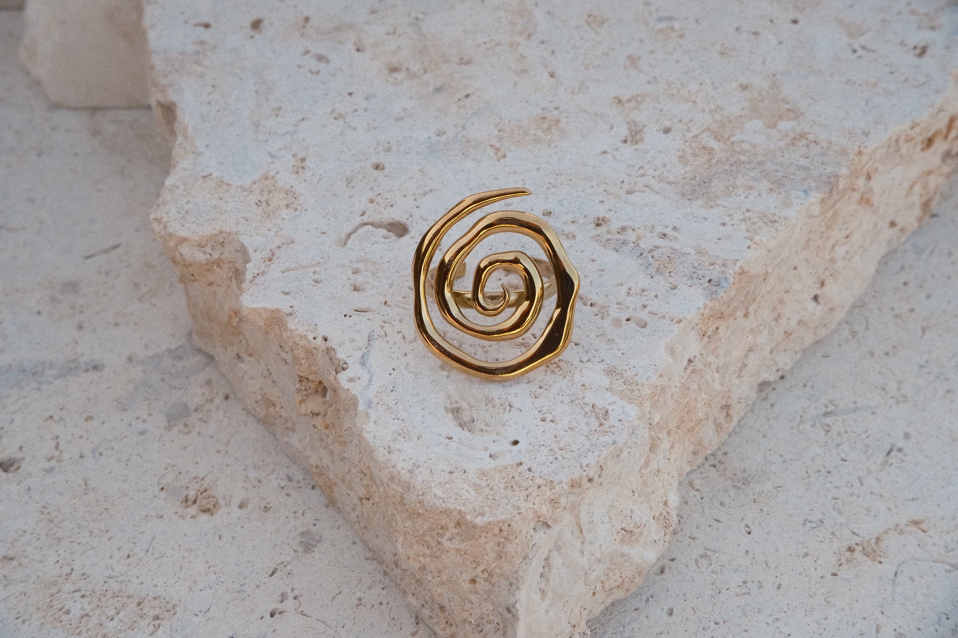 Gold spiral earring on a textured stone surface