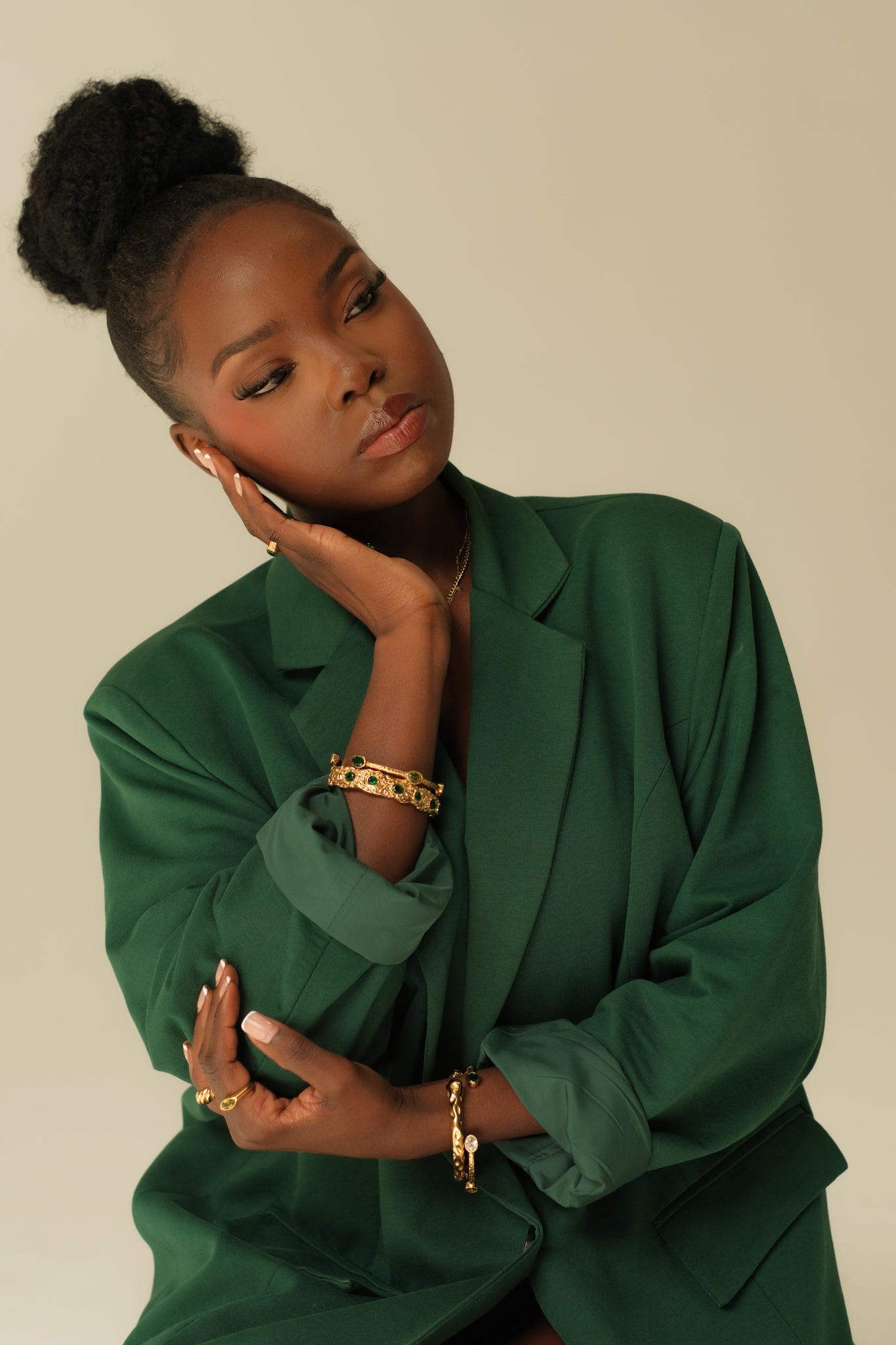 Woman wearing a green outfit with gold jewelry against a beige background