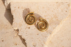 Gold spiral earrings on a textured beige stone surface