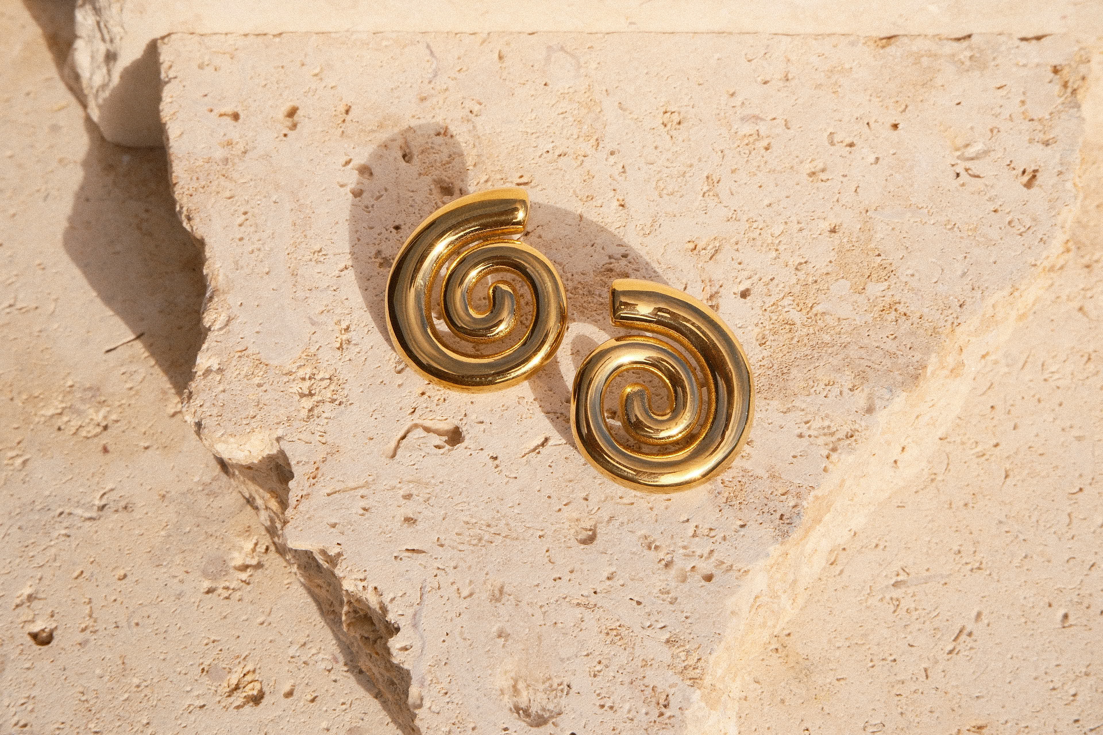 Gold spiral earrings on a textured beige stone surface