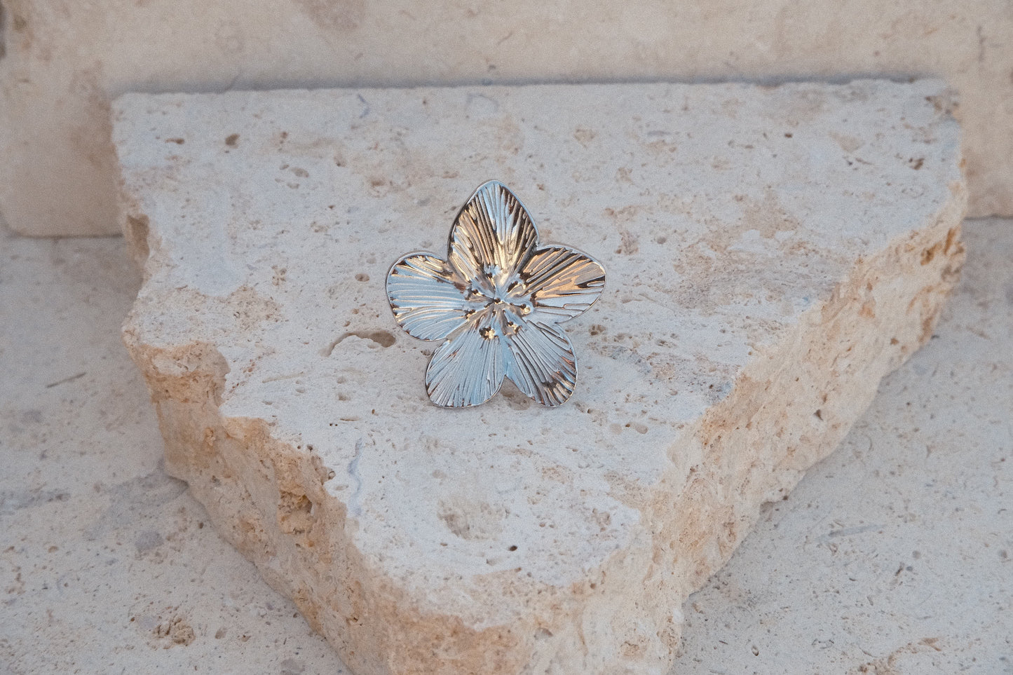 Silver flower-shaped ring on a textured stone surface