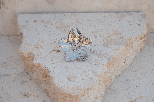 Silver flower-shaped ring on a textured stone surface