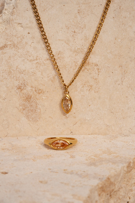 Gold necklace with a pendant on a beige stone surface