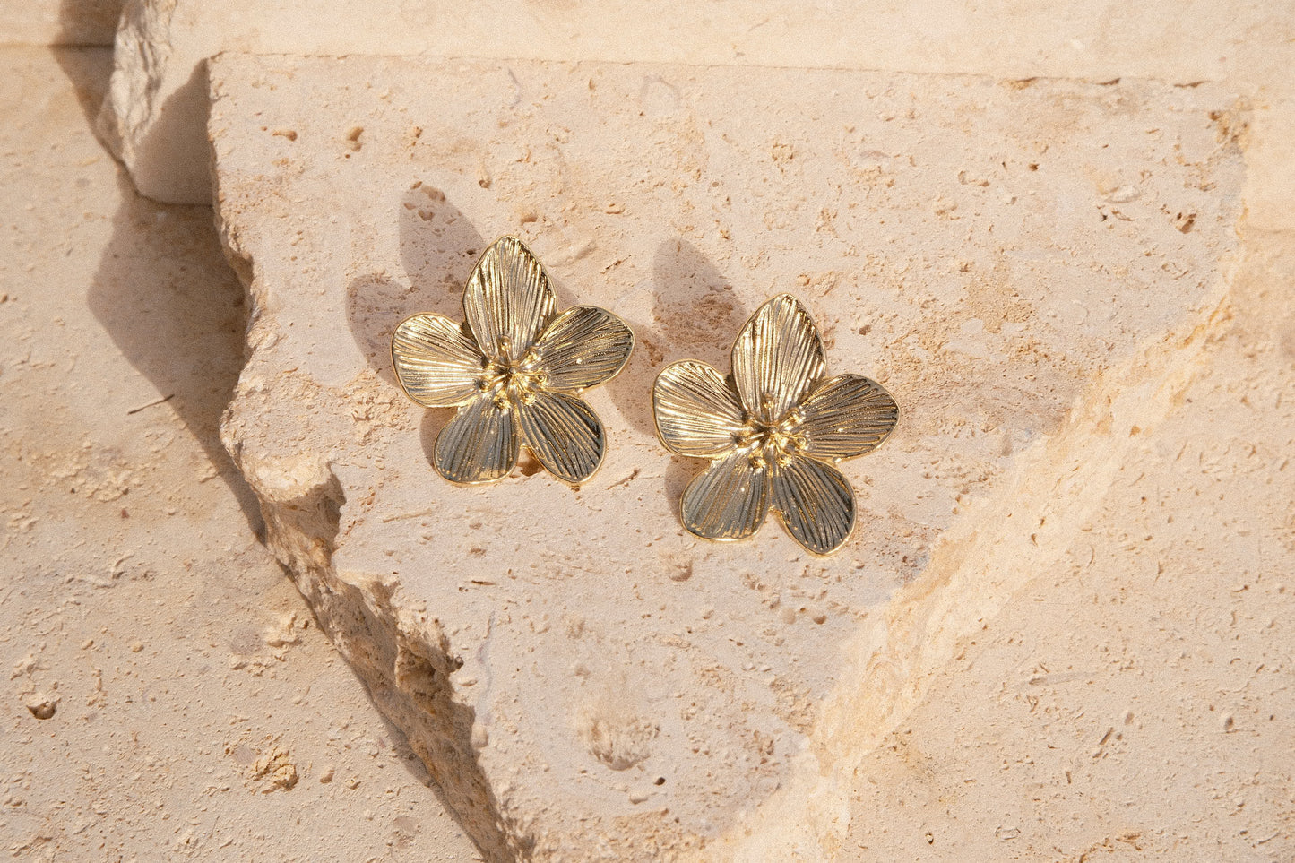 Gold floral earrings on a textured beige stone surface