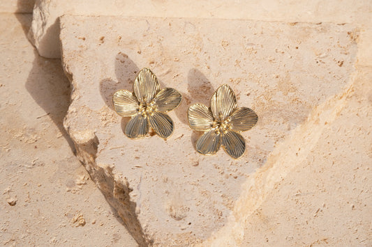 Gold floral earrings on a textured beige stone surface