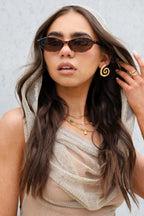 Woman wearing sunglasses and a beige scarf with a neutral background