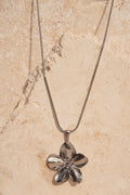 Silver flower-shaped pendant on a chain against a beige marble background