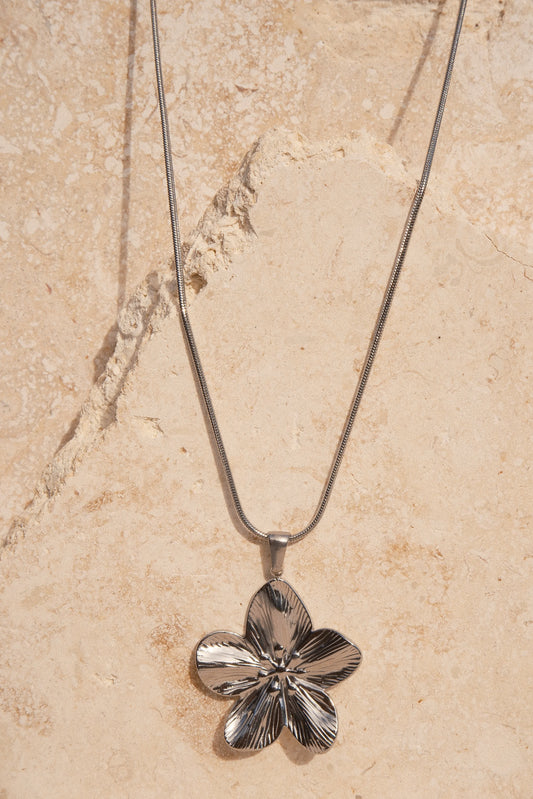 Silver flower-shaped pendant on a chain against a beige marble background