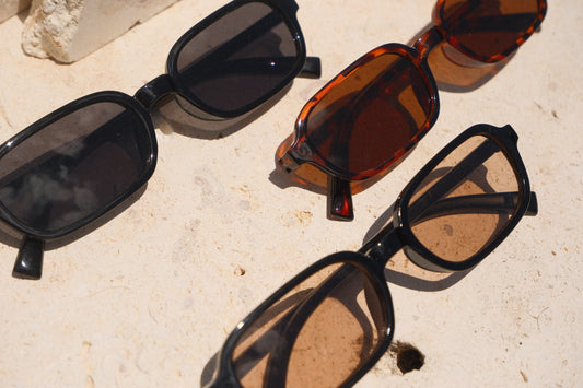 Sol & Aura - Carrie Sunglasses - all three variations of Carrie sunglasses on stone surface. Black with black lens, brown with brown lens and black with tea-coloured lens