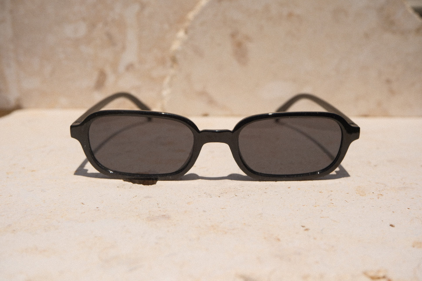 Sol & Aura - Carrie Sunglasses - black rectangular oval sunglasses, front view, on stone surface
