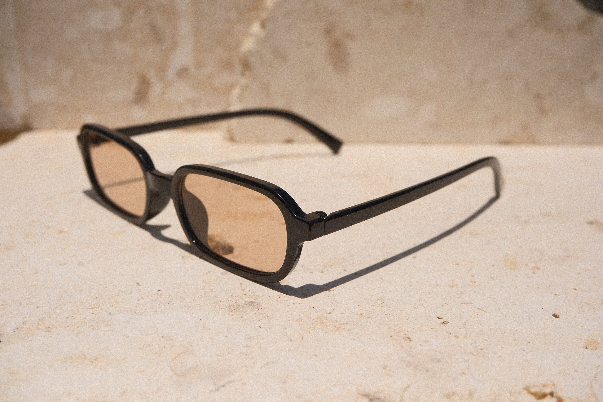 Sol & Aura - Carrie Sunglasses - black frame with tea-coloured lens. Side view on stone surface