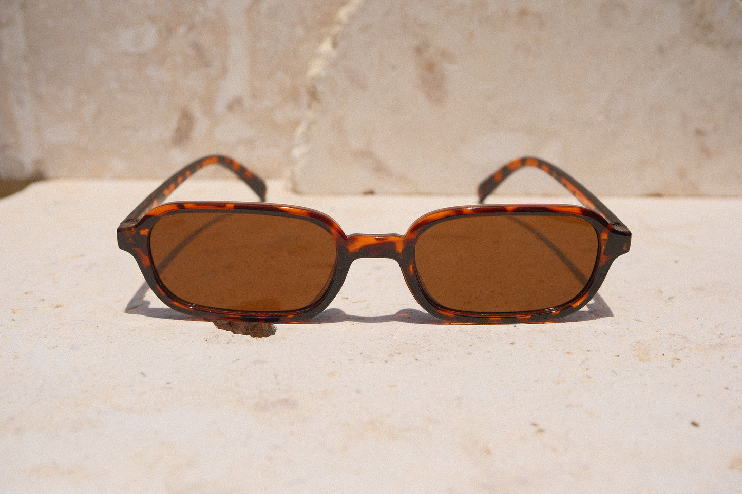 Sol & Aura - Carrie Sunglasses - Brown, tortoise shell detailing. Narrow rectangular lens shape with brown lens on stone surface