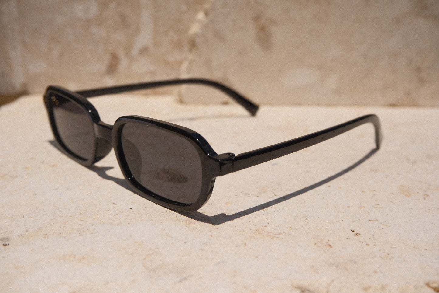 Sol & Aura - Carrie Sunglasses - black rectangular oval sunglasses, side view, on stone surface