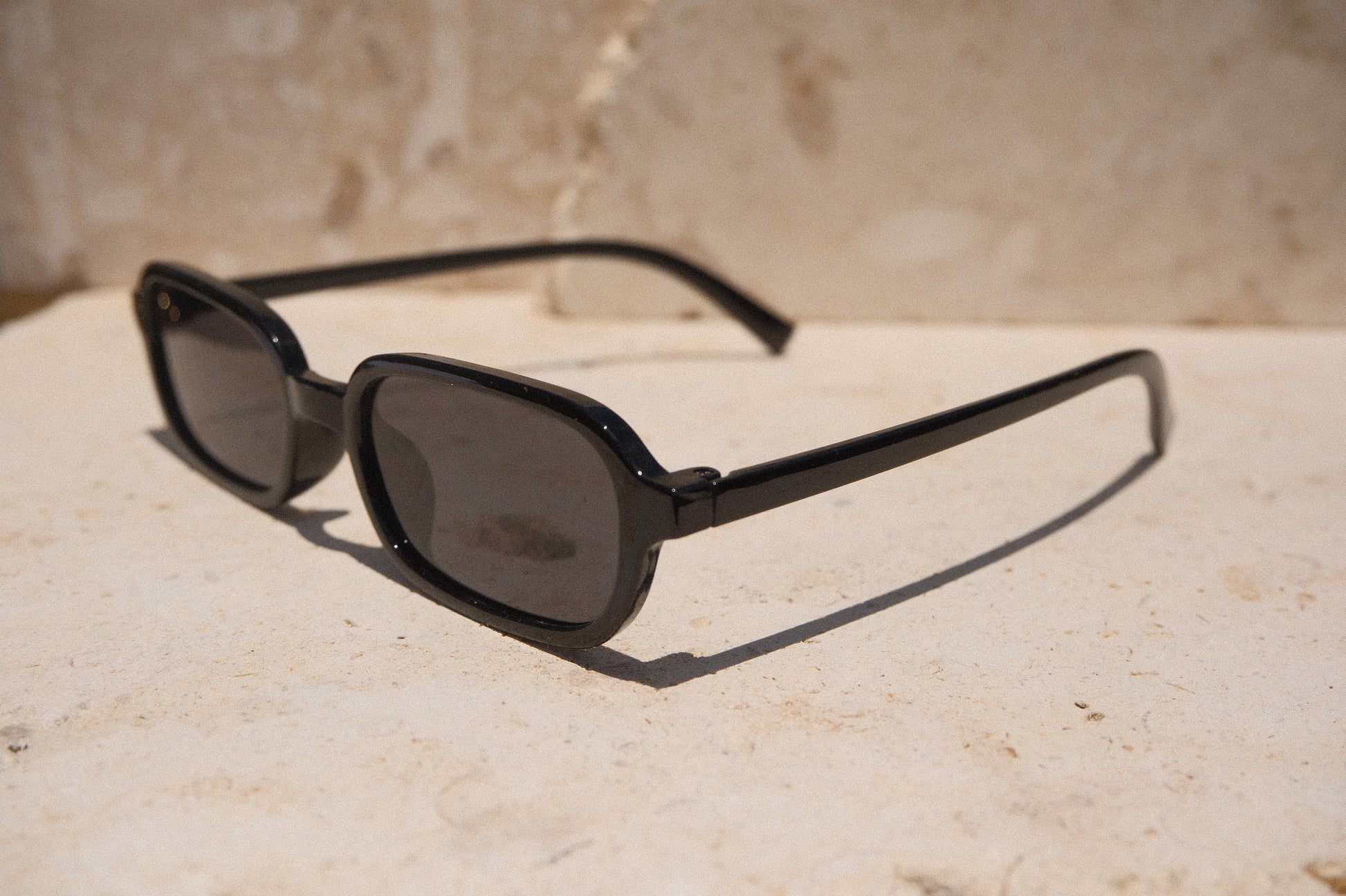 Sol & Aura - Carrie Sunglasses - black rectangular oval sunglasses, side view, on stone surface