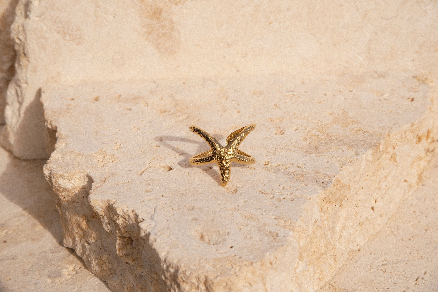 Gold starfish-shaped ring on a textured beige surface