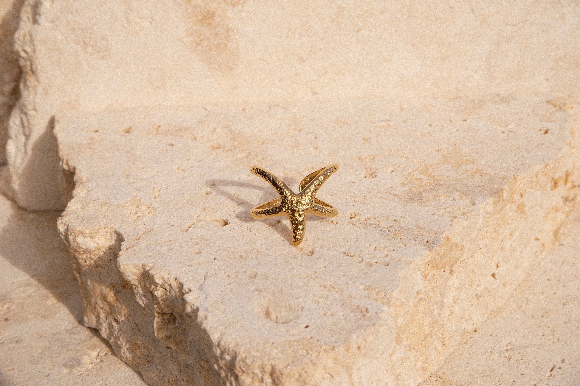 Gold starfish-shaped ring on a textured beige surface
