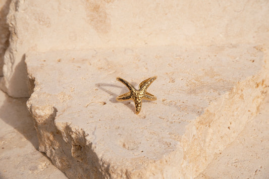 Gold starfish-shaped ring on a textured beige surface