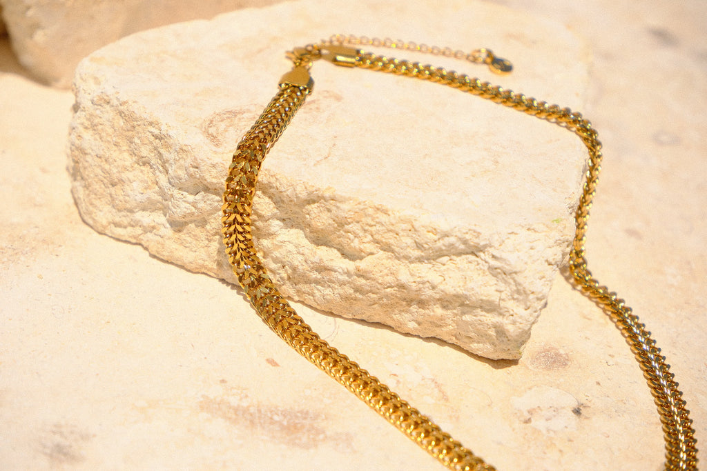 Sol & Aura - Gold chain on natural stone surface with S/A logo