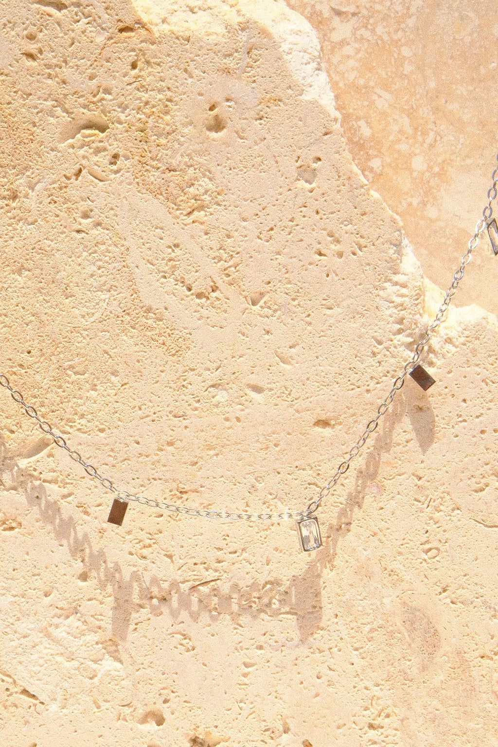 Sol & Aura - Close up of silver necklace with square pendants on a textured stone 