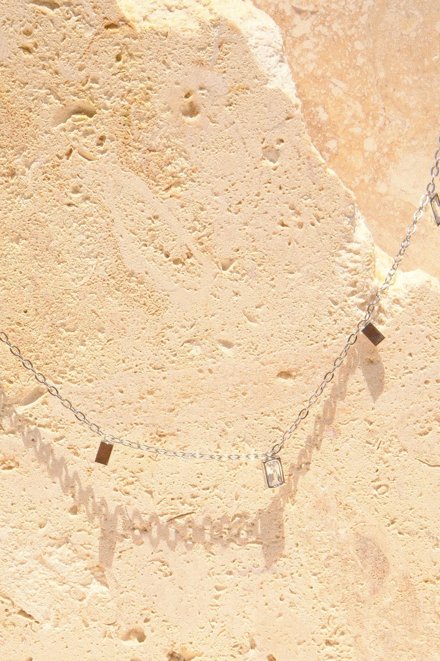 Sol & Aura - Close up of silver necklace with square pendants on a textured stone 