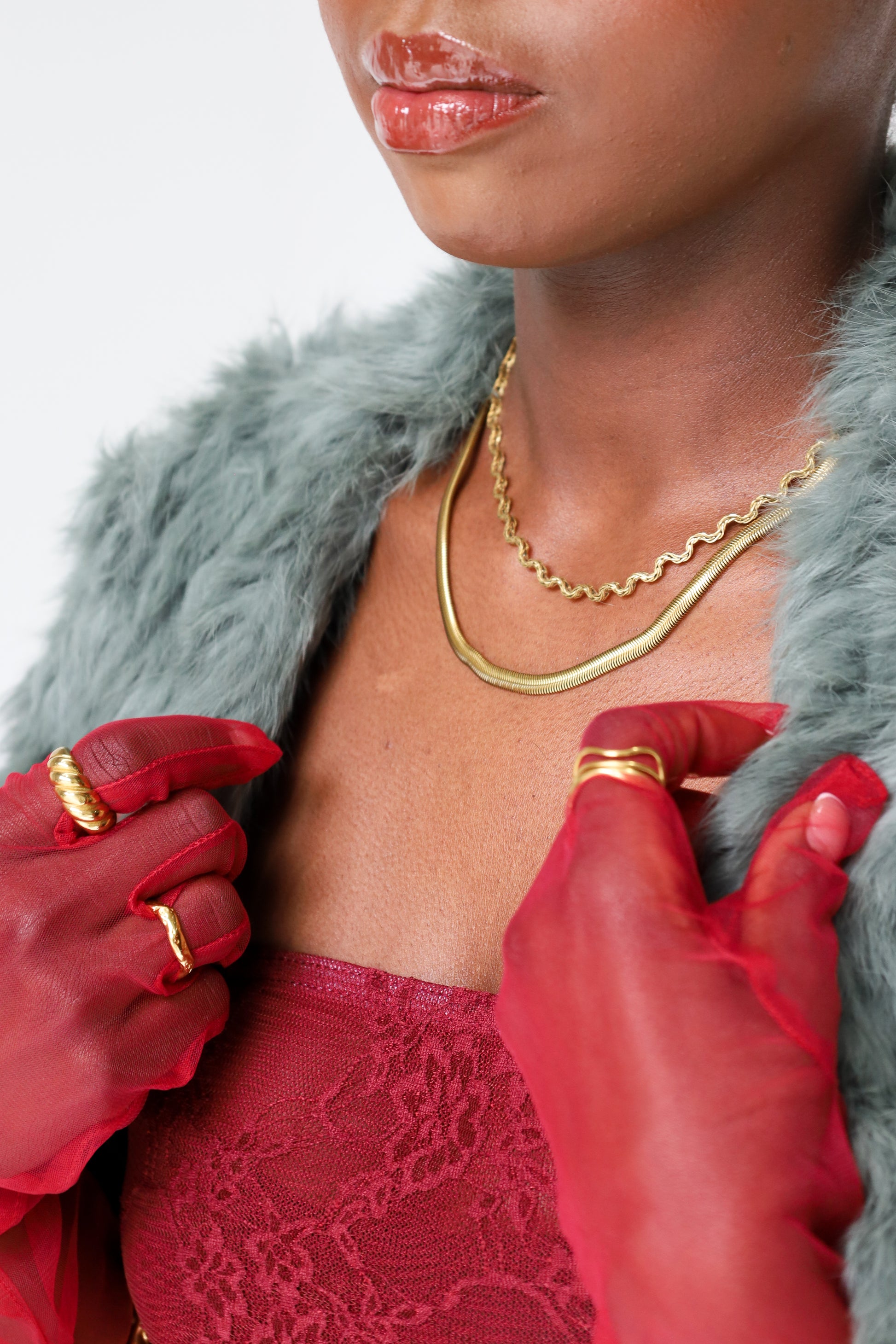 Sol & Aura - close up of coman wearing gold plated jewellery in red lace outfit with sheer red gloves & green fur coat