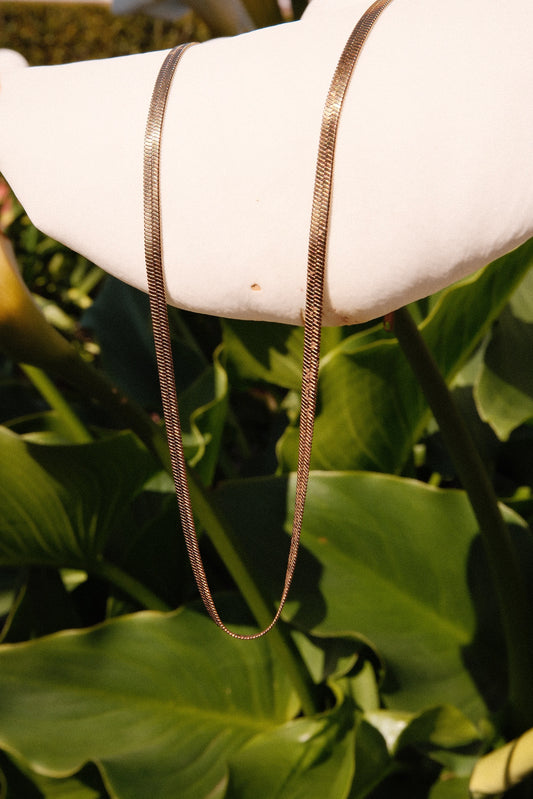 Gold necklace hanging off lily flower in garden with green leaves in the background