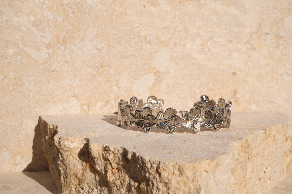 Silver floral bracelet on a stone surface with a beige stone wall background
