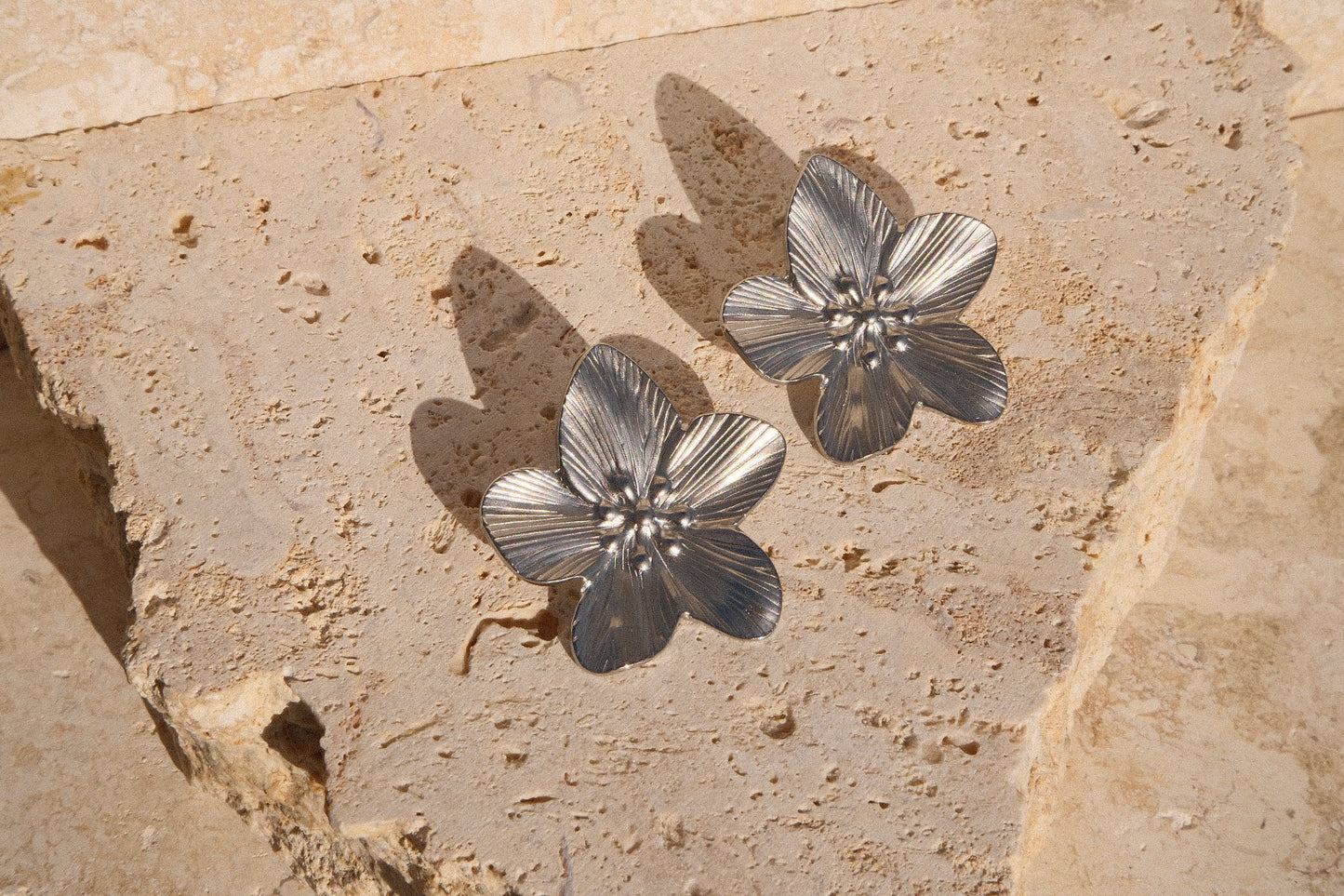 Silver floral earrings on a textured stone surface