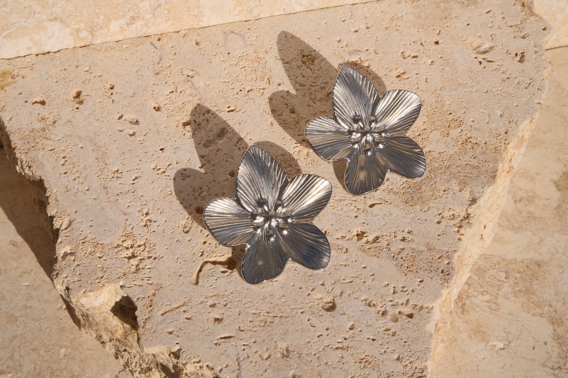 Silver floral earrings on a textured stone surface