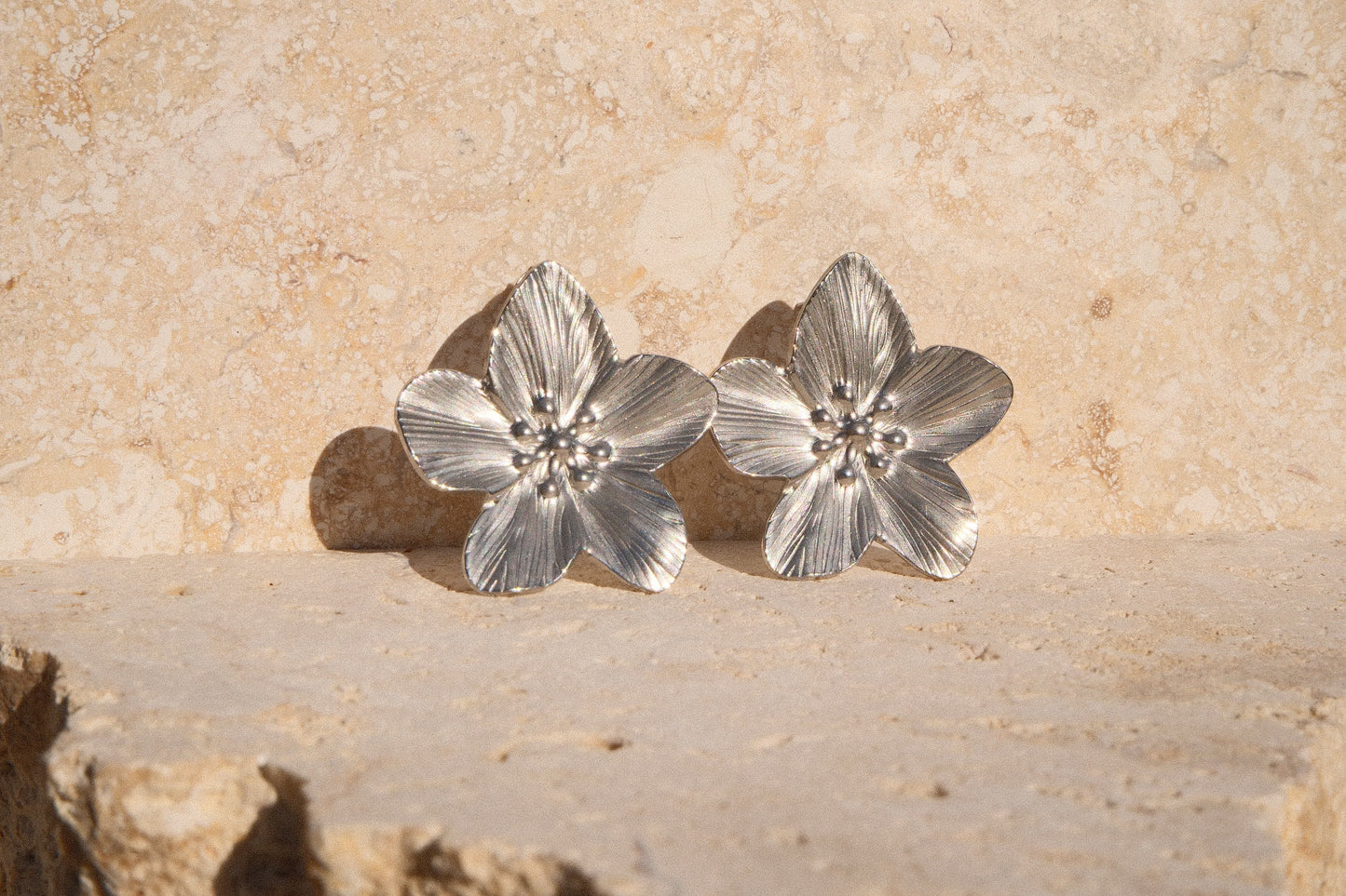Pair of silver flower-shaped earrings on a stone surface
