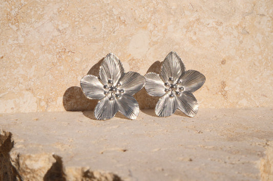 Pair of silver flower-shaped earrings on a stone surface