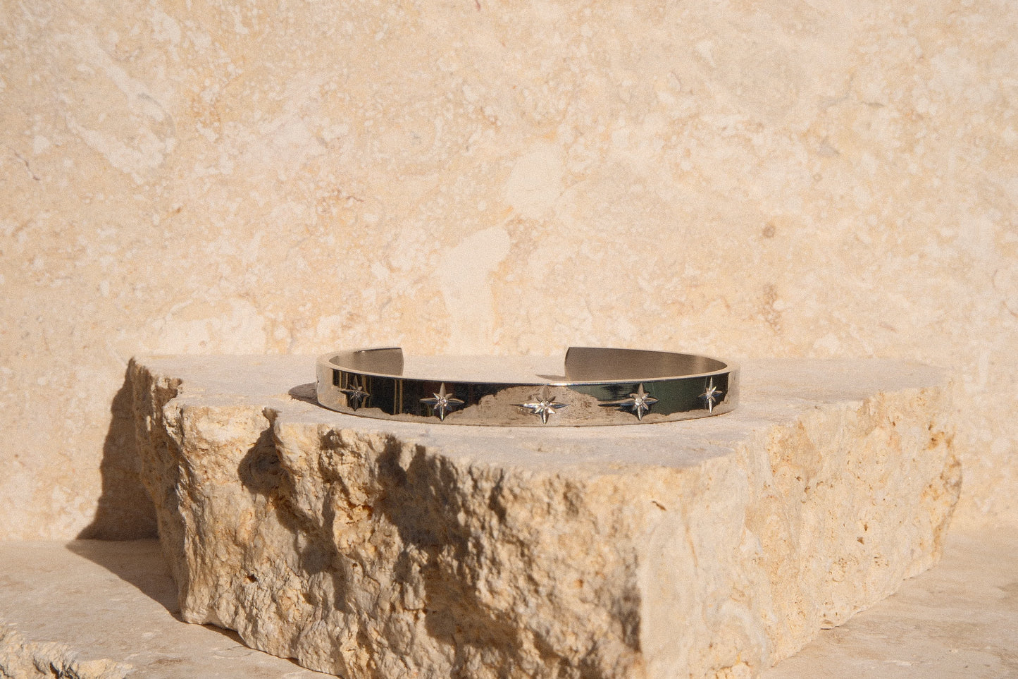 Silver bracelet with star designs on a stone surface against a beige wall.