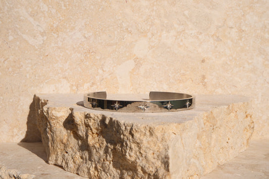Silver bracelet with star designs on a stone surface against a beige wall.