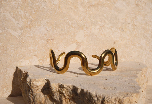 Gold snake-shaped bracelet on a stone surface with a beige background