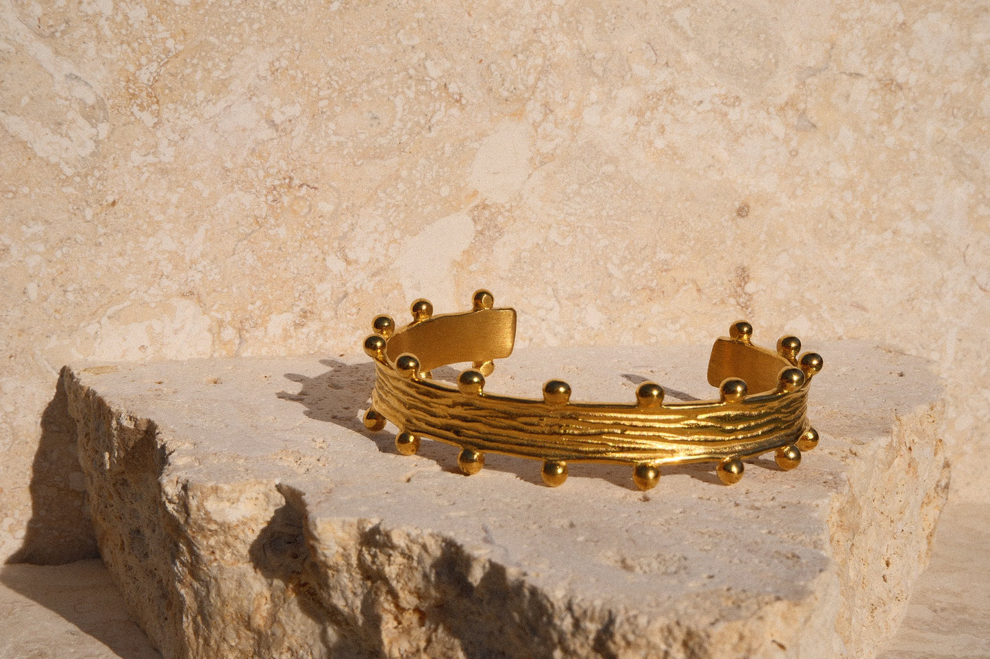 Gold bracelet on a stone surface with a textured beige background