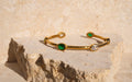 Gold bracelet with green gemstones on a stone surface